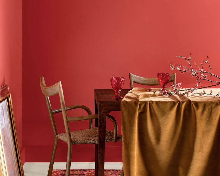 Dining room with coral tinged with pink painted wall, a table, chairs, cups and a branch with buds