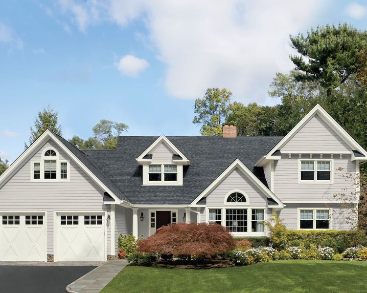 A light gray colored house with vinyl siding and two door garage.